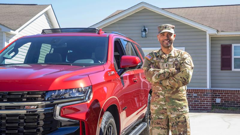Man in army fatigues standing next to a red truck