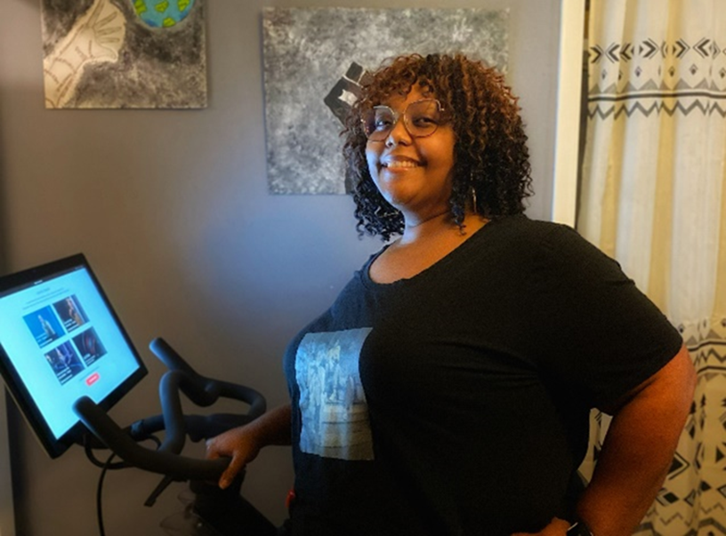 Corvias Property Management Leasing Consultant, Andrea Ruffin poses with the indoor bike she received for participating in Wellness@Corvias.
