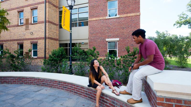 Students sitting on a short brick wall outside of a building