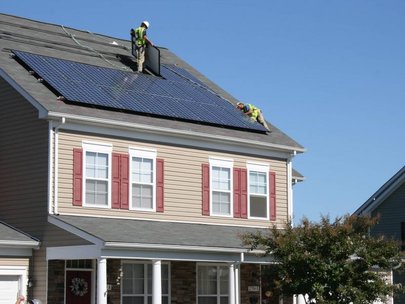 Workers installing solar panels on the roof of a house
